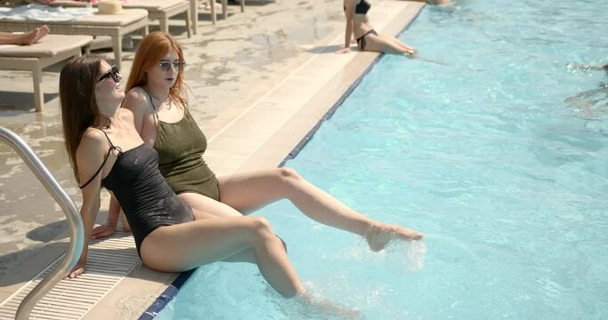 Two girls relaxing at outdoor swimming pool with blue water