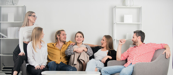 Group of young people sitting on sofa and talking at home. Young friends having a great time in...