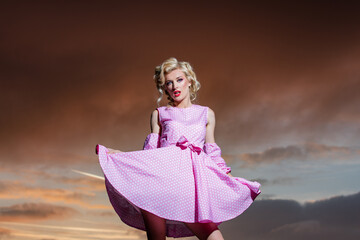 Pinup style woman in summer dress on dramatic sky. Beautiful girl in stylish fashion clothes in...