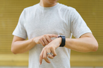 Active Asian young sportsman using a smartwatch or smart fitness band to track his outdoor workout and activities.