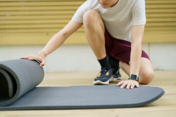 Active Asian sportsman unroll an exercise mat on the floor.