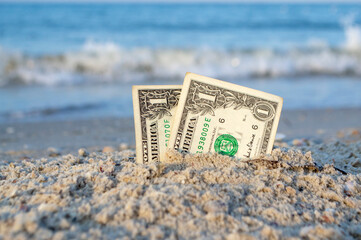 Two one dollar bills half buried in sand on sandy seashore close-up. Two paper dollar bills half in...