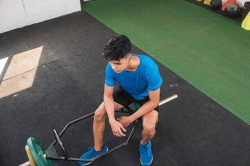 A young man sulks while sitting on a trap bar at the gym. In deep thought while staring blankly....