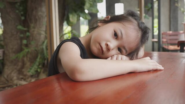 Close up face of adorable asian girl kid who is sleeping alone on the table shows concept of tired and bored child alone for her stress from school or family, and need to be rest and relax. 
