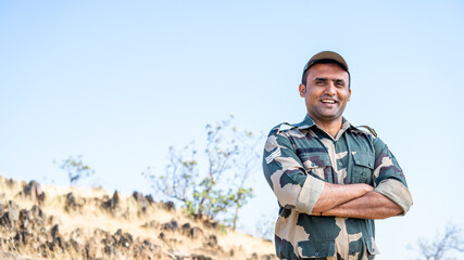 Confident smiling indian soldier in uniform standing with arms crossed by looking at camera - concept of successful, proud serviceman and occupation.