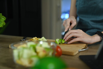 Woman cutting fresh organic apple on wooden board while preparing ingredients for making healthy salad in kitchen.