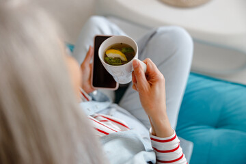 Close up of female hands holding cup of tea with lemon and modern smartphone