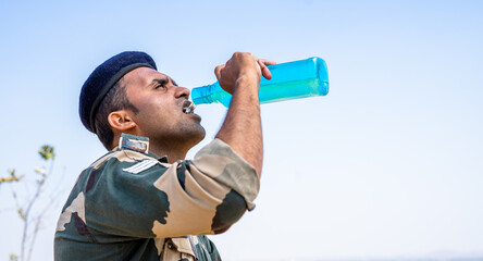 Thirsty solider drinking water while on top of mountain during hot sunny day - concept of taking...