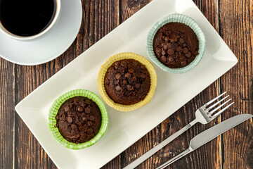 Chocolate chip and cocoa muffins in colorful muffin paper molds on wooden table