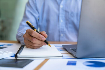 Businessman sitting at desk using laptop and taking notes, analyzing financial data and graphing market growth reports. and investment results, analytical concepts and financial investments.