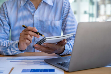 Businessman sitting at desk using laptop and taking notes, analyzing financial data and graphing market growth reports. and investment results, analytical concepts and financial investments.