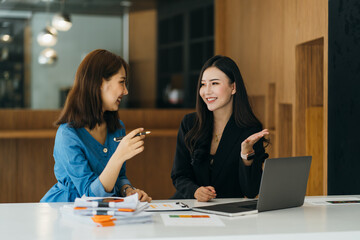 Two young women working together in an office at their small business sitting reading a report or paperwork with pleased smiles