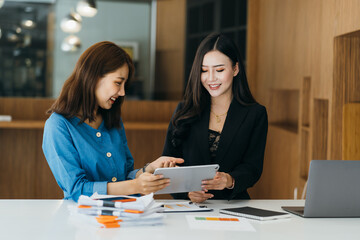 Close up happy young asian businesswoman using laptop with laughing female mentor in coworking boardroom at meeting. Smiling diverse woman managers talking about new business concept.