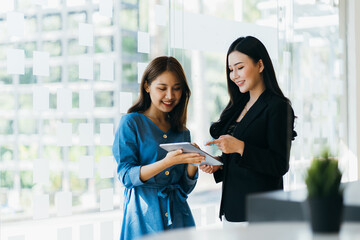 Smiling businesswoman holding digital tablet and talking with partner while standing in modern...