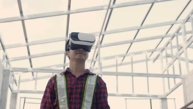 Asian architect engineer worker man in protective helmet and uniform using VR gear glasses to visualize planning and development projects while working at the house building construction site