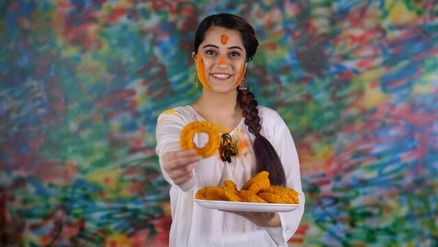 A pretty Indian girl with braided hair wishing people a Happy Holi with a traditional Gujiya - an Indian sweet  sweet delicacy  a tasty cuisine. A beautiful lady in a white Kurti celebrating the In...