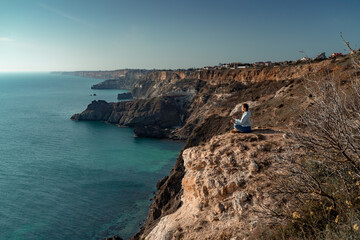 Fototapeta na wymiar Woman tourist enjoying the sunset over the sea mountain landscape. Sits outdoors on a rock above the sea. She is wearing jeans and a blue hoodie. Healthy lifestyle, harmony and meditation