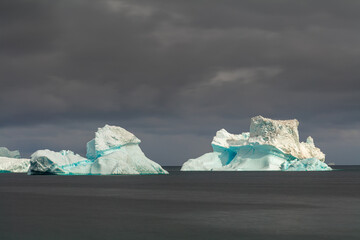 Long exposure image of icebergs floating in the sea off the coast of Disko Island, Greenland under dark overcast sky
