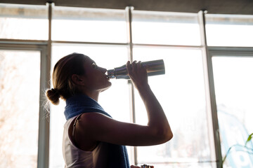 The silhouette of a girl drinks water from a bottle during a workout. A sports woman holds a...