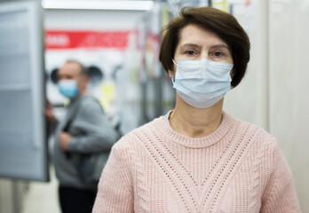 Portrait of middle aged caucasian woman in face mask standing in appliance store.