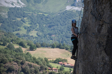 Chica subiendo por una via ferrata con las montañas al fondo