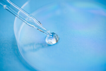 Dropper pipette with serum or cosmetic liquid and petri dish on blue background. Transparent container with liquid and bubbles. The appearance of the texture of the gel. Medicine and beauty concept.