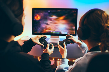 Friends playing video game at home. Gamers holding gamepads sitting at front of screen. Streamers...