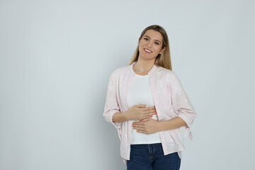 Happy woman touching her belly on light background, space for text. Concept of healthy stomach