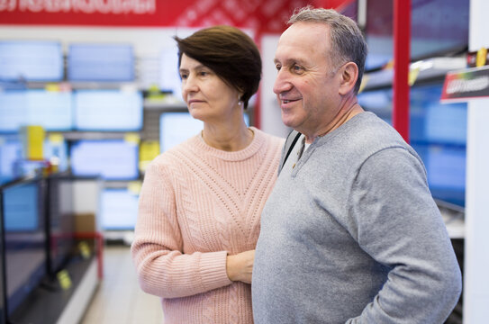 Portrait of a mature European couple in an electronics and home appliance store, standing in the department with televisions