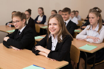 Happy schoolchildren sit at a desk in the classroom