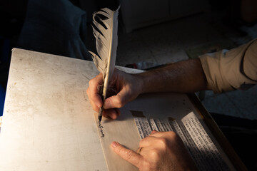 Closeup view of the hands of a Jewish scribe holding a feather quill and writing the words of the Shema Yisrael prayer on parchment for a mezuzah that will be placed on the door of a Jewish home. - obrazy, fototapety, plakaty