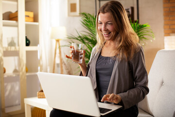 Girl holding a glass of water. Smiling girl drinking water while using the laptop.