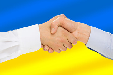 political, business and national concept - close up of handshake over colors of flag of ukraine on background