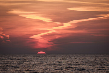 sun setting in the sea with cloud trails