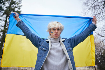 Caucasian man holding Ukrainian flag stretched and looking at camera