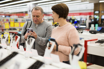 Middle aged wife and husband picking new smartphone in electronic store.