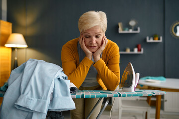 Tired old woman front of ironing board