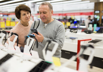 Fototapeta premium European man who came to an electronics store with his wife chooses a mobile phone to buy it