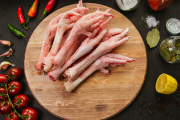 Poultry meat. Turkey legs lie on a wooden board. Chicken legs with peppers and tomatoes on a black background.