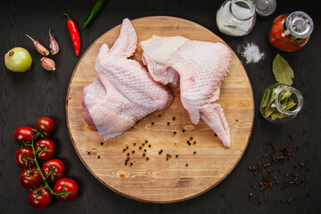 Poultry meat. Turkey wings lie on a wooden board. Chicken wing with peppers and tomatoes on a black...