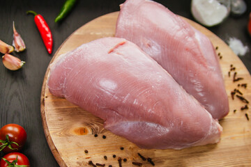 Poultry meat. Turkey fillets lie on a wooden board. Chicken breast with peppers and tomatoes on a black background.