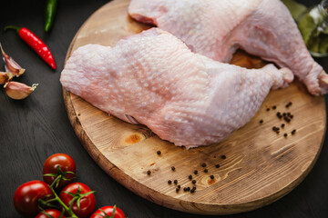 Turkey legs lie on a wooden board. Chicken thigh with peppers and tomatoes on a black background