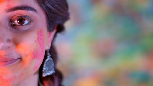 A pretty lady wearing beautiful earrings posing for the camera at the Holi festival. A young woman smeared with Gulal / Abeer on her face enjoying the Indian festival of colors - festive season  a ...