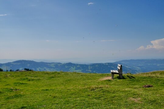 Wooden bench at Niedere in Bregenzerwald, paragliders in the sky. Vorarlberg, Austria.