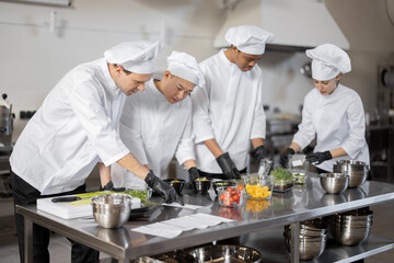 Fototapeta na wymiar Multiracial team of cooks mixing ingredients for take away food in professional kitchen. Concept of dark kitchen for cooking for delivery. Idea of teamwork in a restaurant. Diverse people at job