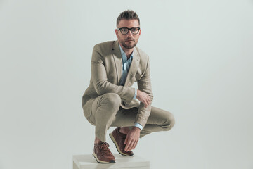 handsome unshaved man in his 40s with elbow on knee crouching