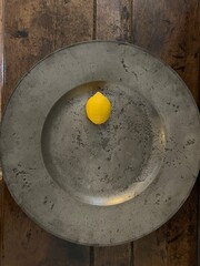 Close up of single yellow lemon, the citrus fruit on it own on a large silver pewter serving platter flat dish with the background of the wood ancient table interior flat lay view