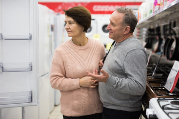 European spouses of mature age, who have come to the electronics and household appliances store for shopping, choose a ..refrigerator, examining it