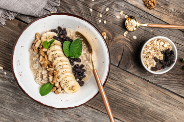 Oatmeal. Porridge with dried raisins, banana and walnuts decorated with mint for healthy breakfast or lunch. Natural ingredients. Clean eating, dieting, vegan food concept. top view