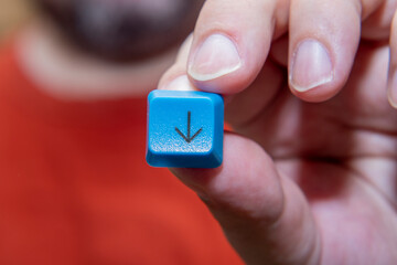 Close-up of a man's hand with a button from the keyboard. Blue plastic button with down arrow